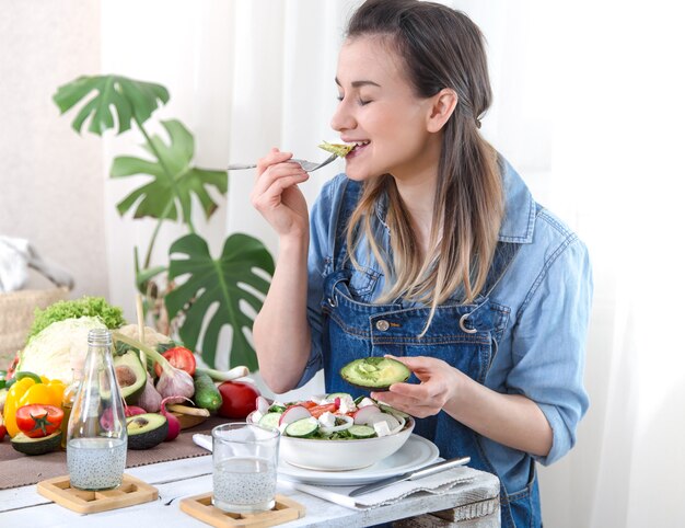 Mujer joven y feliz comiendo ensalada en la mesa