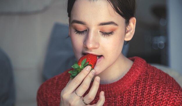 Mujer joven feliz comiendo fresas en casa