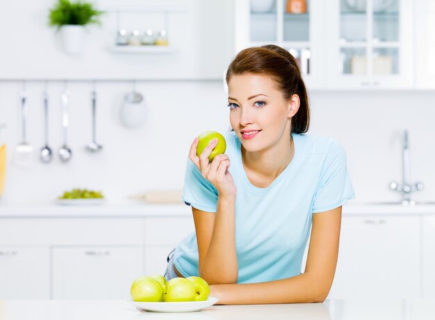 Mujer joven feliz comiendo manzanas en la cocina