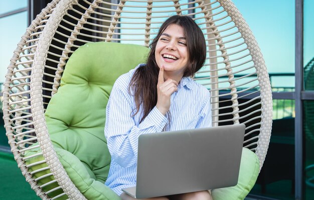 Mujer joven feliz con computadora portátil trabaja de forma remota en una hamaca