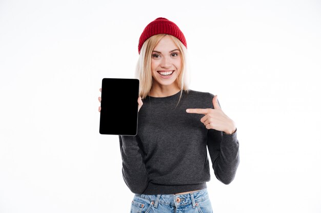 Mujer joven feliz en dedo acusador del sombrero en la tableta de la pantalla en blanco