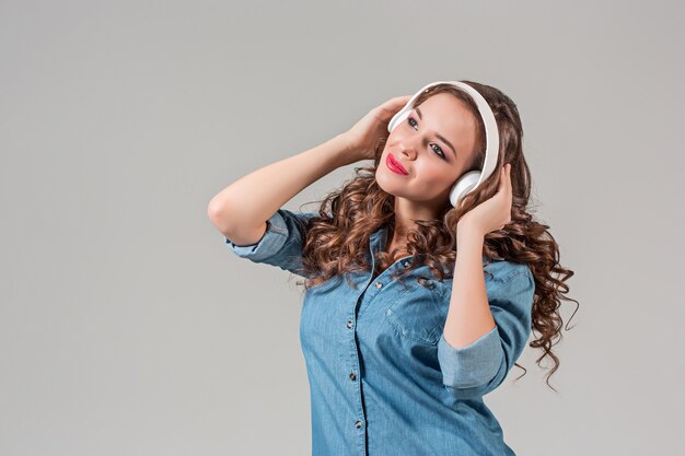 Mujer joven feliz escuchando música con auriculares. Retrato aislado en pared gris