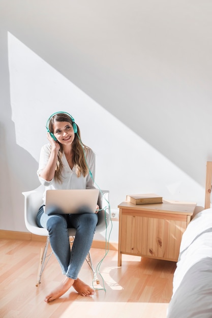 Mujer joven feliz escuchando música en el portátil