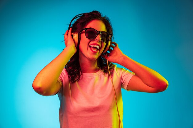 Mujer joven feliz escuchando música y sonriendo sobre moderno estudio de neón azul