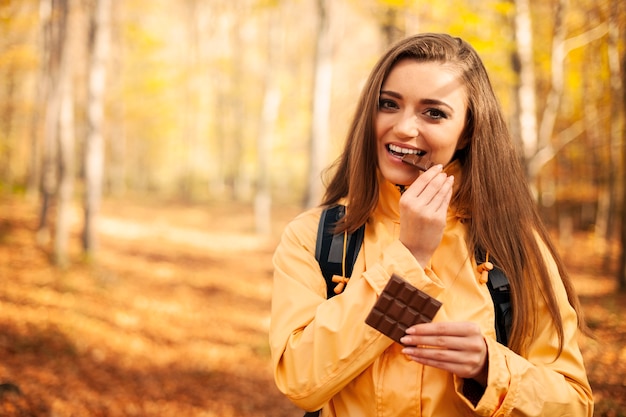 Foto gratuita mujer joven feliz excursionista comiendo chocolate