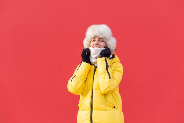 Mujer joven feliz en el fondo de una pared roja en ropa de abrigo en un día soleado de invierno