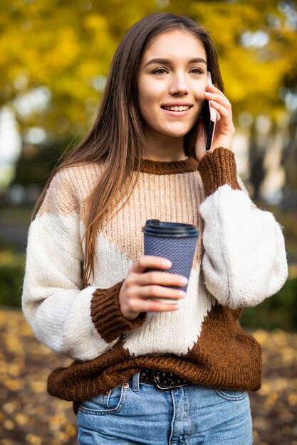 Mujer joven feliz hablando por teléfono, sosteniendo una taza de café para llevar y sonriendo.