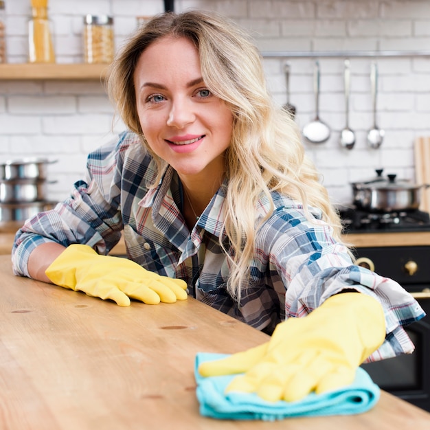Mujer joven feliz limpiando el mostrador de la cocina con guantes amarillos