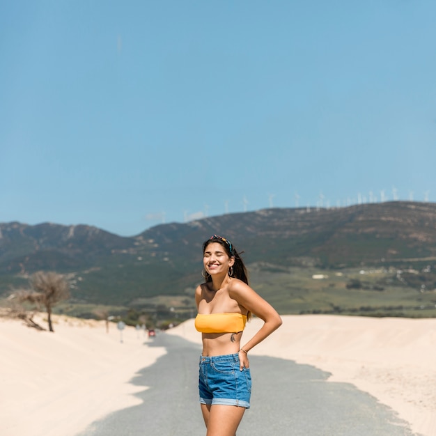 Mujer joven feliz en luz del sol en el camino arenoso