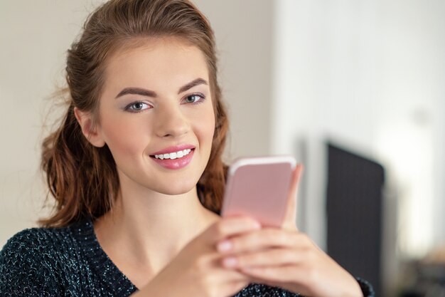 Mujer joven feliz mirando su teléfono inteligente en casa. Mensaje de tipos de mujer en su teléfono inteligente.