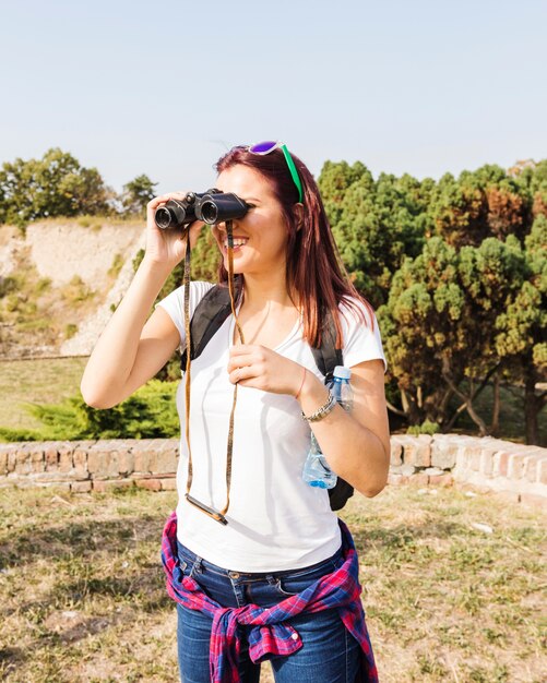 Mujer joven feliz mirando a través de binoculares al aire libre