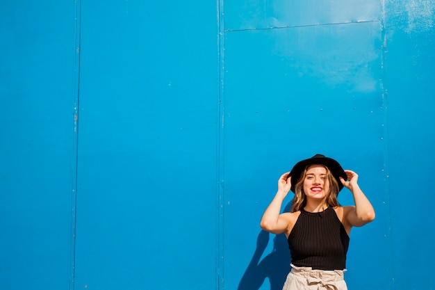 Mujer joven feliz de pie contra la pared azul