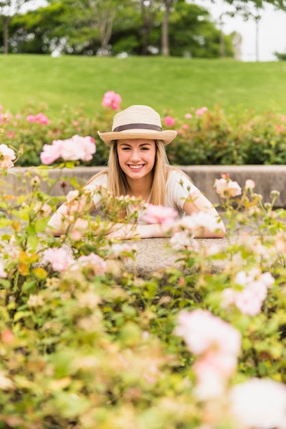 Mujer joven feliz que se coloca en parque cerca de las flores