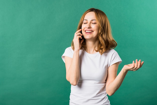 Mujer joven feliz que habla en el teléfono celular contra fondo verde