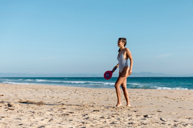 Mujer joven feliz que juega a tenis en la costa