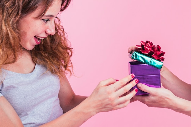 Foto gratuita mujer joven feliz que mira el asimiento abierto de la caja de regalo de su amigo contra fondo rosado