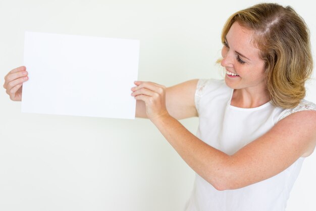 Mujer joven feliz que muestra la hoja de papel en blanco