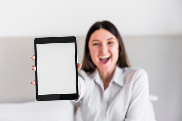 Mujer joven feliz que muestra la tableta digital de la pantalla blanca