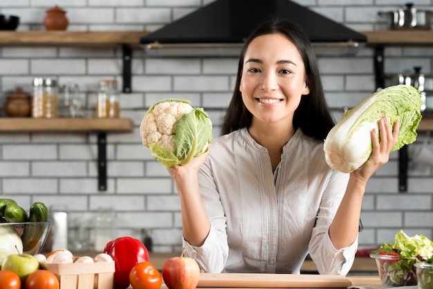 Foto gratuita mujer joven feliz que muestra verduras frescas en cocina