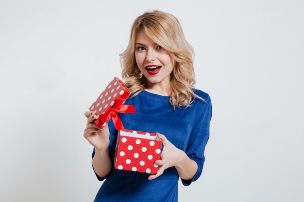 Mujer joven feliz que sostiene la caja de regalo sobre la pared blanca