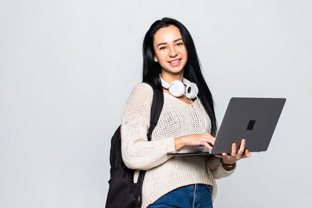 Mujer joven feliz que sostiene la computadora portátil y sobre la pared gris