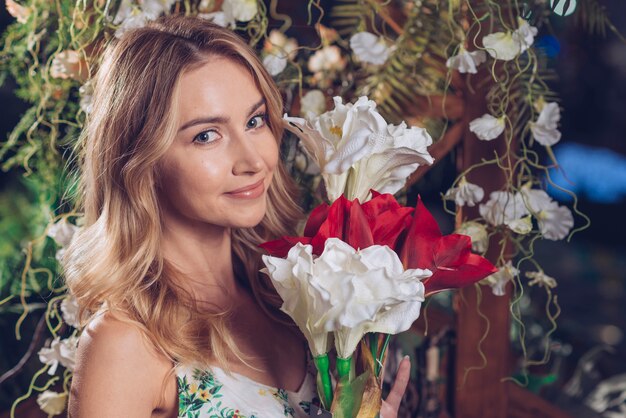 Mujer joven feliz que sostiene el manojo de flores blancas y rojas artificiales