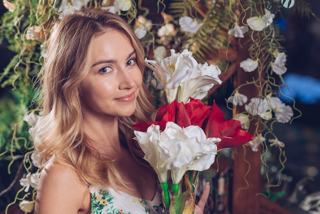 Mujer joven feliz que sostiene el manojo de flores blancas y rojas artificiales