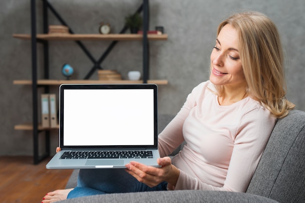 Mujer joven feliz que sostiene mirarla un ordenador portátil abierto que muestra la pantalla de visualización blanca