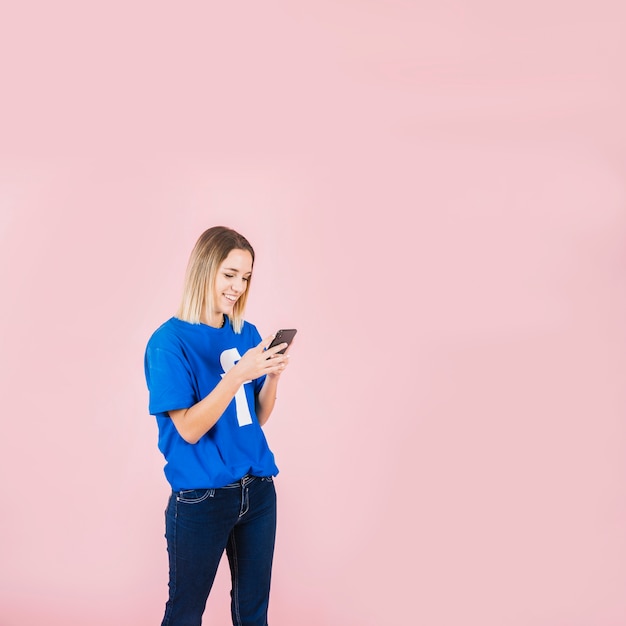 Foto gratuita mujer joven feliz que usa el teléfono móvil en fondo rosado