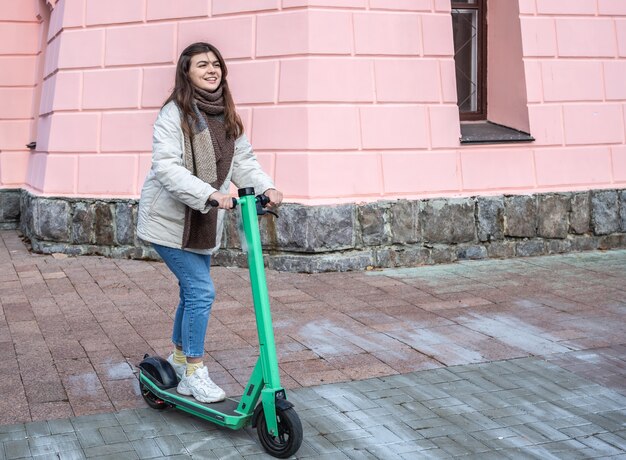 Mujer joven feliz en scooter eléctrico en la ciudad.