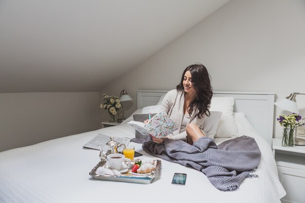 Mujer joven feliz sentada en la cama y escribiendo