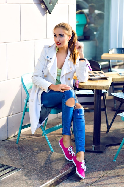 Mujer joven feliz sonriendo y relajándose en la terraza del café de la ciudad, clima soleado, maquillaje brillante, atuendo casual con estilo, vacaciones, viajes, vacaciones, alegría.