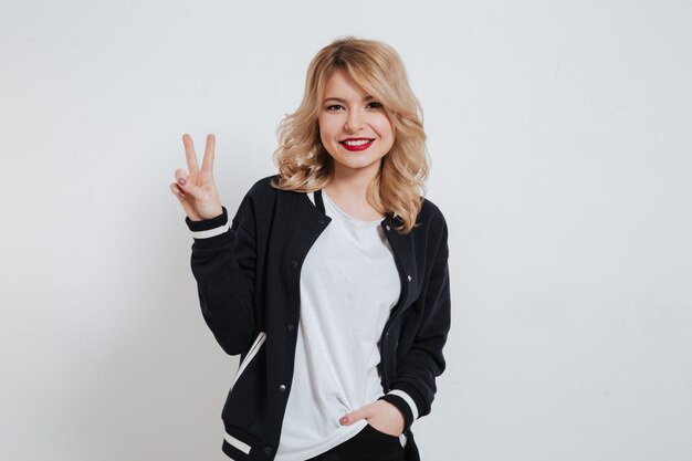 Mujer joven feliz sonriente en ropa casual que muestra gesto de paz