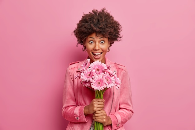 Mujer joven feliz sorprendida con el pelo afro tiene hermosas flores de gerbera