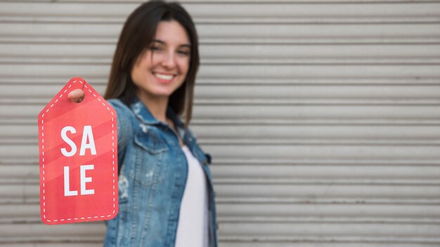 Mujer joven feliz con la tableta de la venta cerca de la pared que cubre perfilada