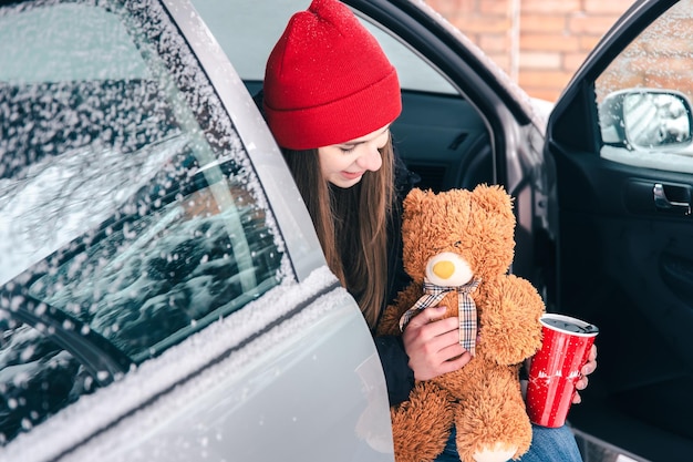 Mujer joven feliz con una taza termo roja se sienta en un coche en invierno