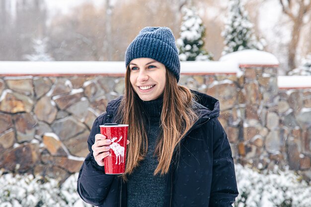 Mujer joven feliz con taza termo en tiempo de nieve