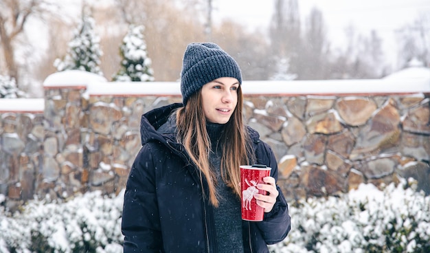 Mujer joven feliz con taza termo en tiempo de nieve