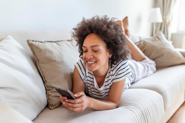 Mujer joven feliz con teléfono móvil tendido en el sofá