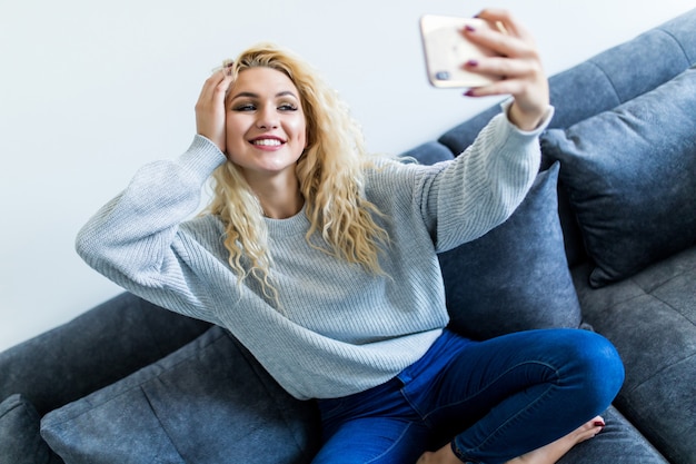 Mujer joven feliz tomando selfie con su teléfono mientras está sentado en la sala de estar.