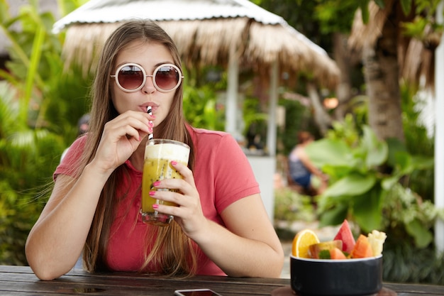 Mujer joven feliz de vacaciones bebiendo bebida fresca. Atractiva mujer caucásica en tonos redondos de moda bebiendo cócteles sin alcohol