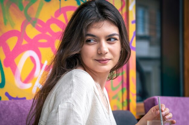 Mujer joven feliz con un vaso de limonada contra una pared pintada brillante