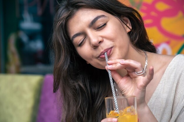 Mujer joven feliz con un vaso de limonada contra una pared pintada brillante