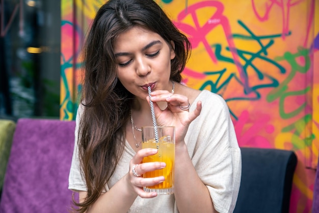 Mujer joven feliz con un vaso de limonada contra una pared pintada brillante