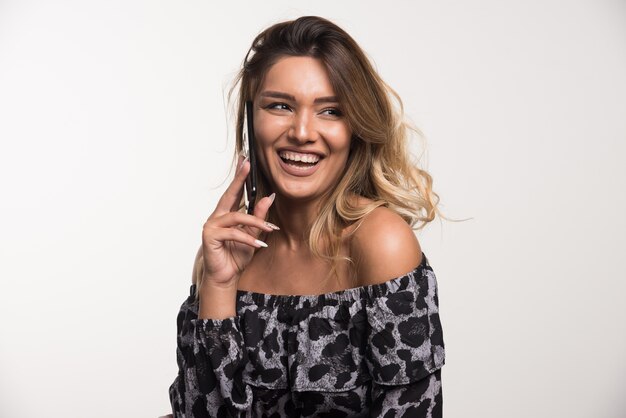 Mujer joven felizmente hablando con teléfono en la pared blanca.