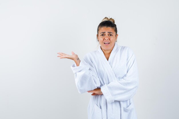 Mujer joven fingiendo mostrar algo en bata de baño y mirando indefenso