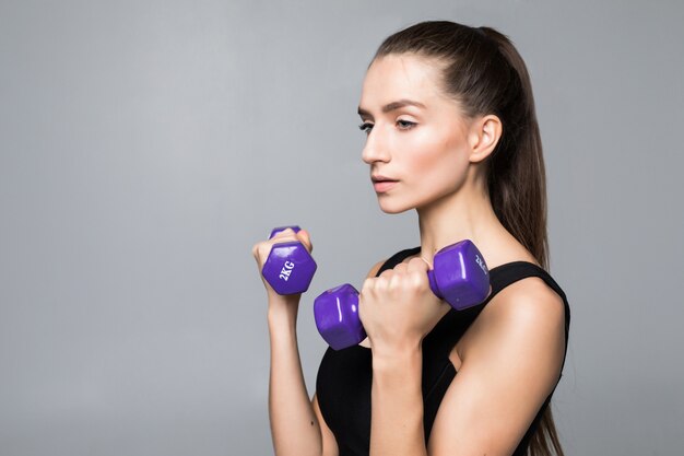 Mujer joven fitness ejercicio con pesas aislado en la pared blanca