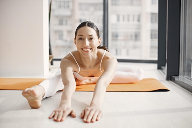 Mujer joven fitness haciendo estiramientos de yoga en una alfombra en el estudio con grandes ventanales