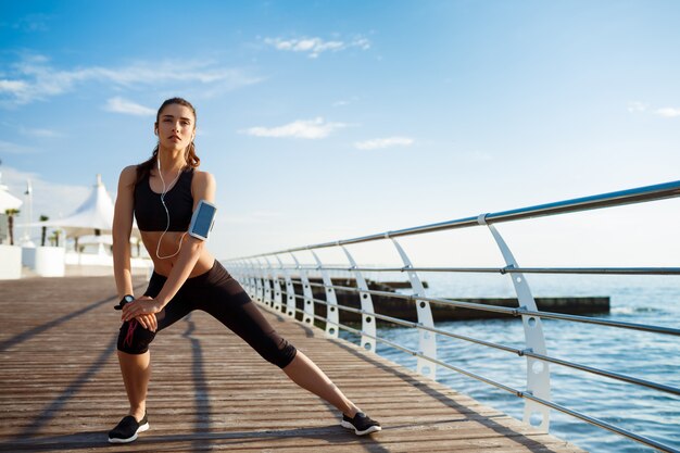 Mujer joven fitness que hace ejercicios deportivos con la costa del mar detrás