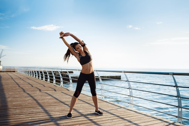 Mujer joven fitness que hace ejercicios deportivos con la costa del mar detrás